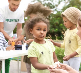 Volunteers giving vitamin tablets to poor African children outdoors